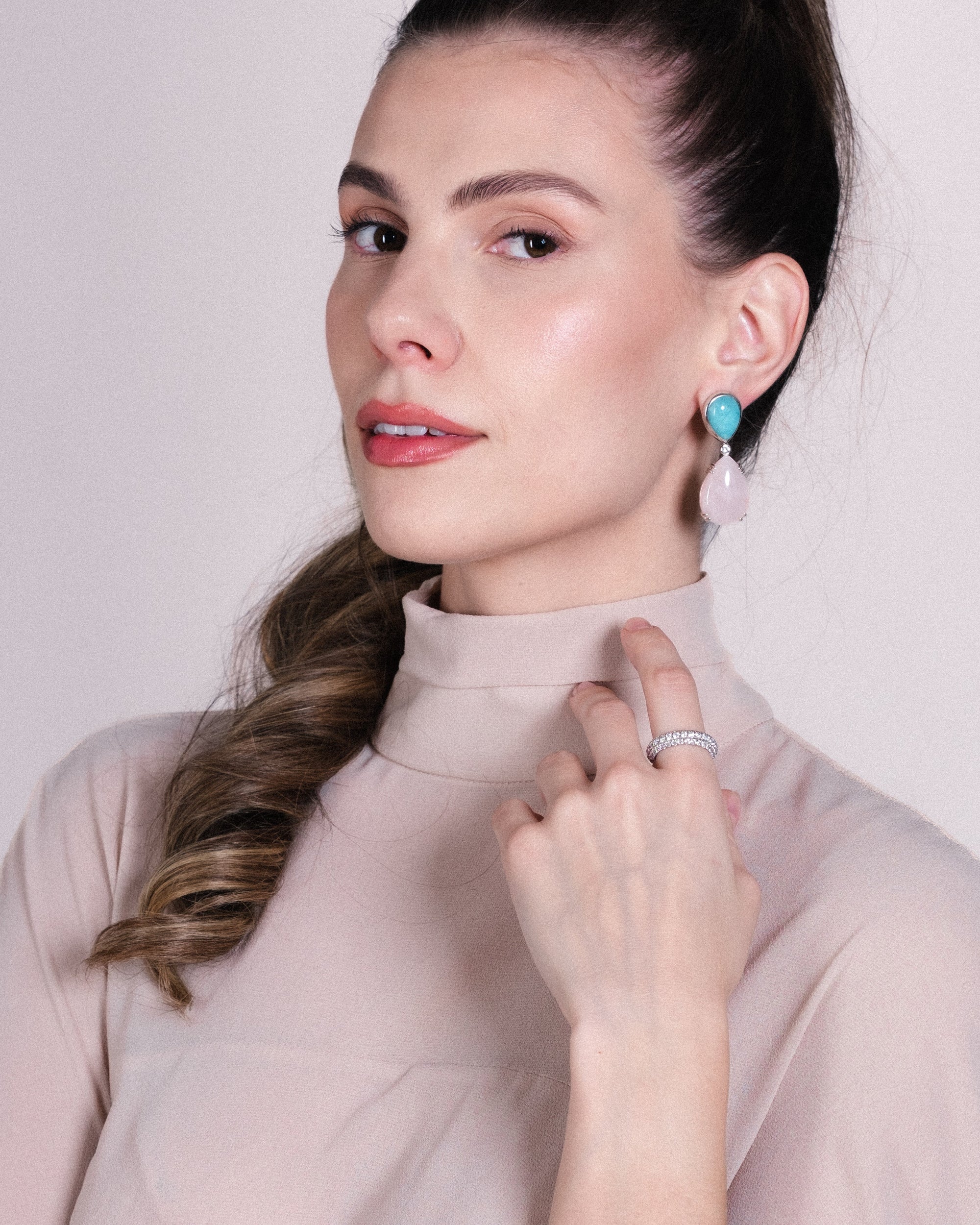 Woman wearing turquoise earrings and a ring, against a plain background